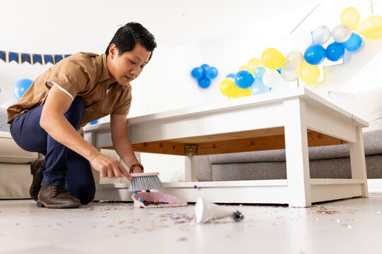Father cleaning party mess with brush and dustpan in living room, at home