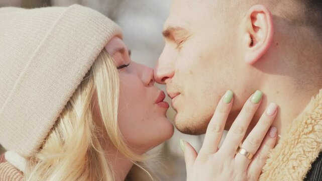 Happy couple in love with coffee in hands walking outdoors in winter. Woman looks at man with love and kisses him.