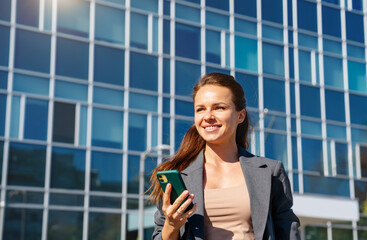 Fototapeta premium Successful urban woman with mobile phone in her hand outdoors on city street.