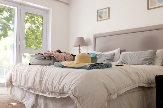Open suitcase and sun hat on bed in bright, cozy bedroom, at home