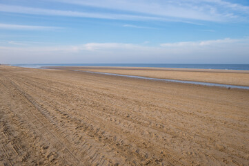 Tire tracks covering sandy beach by the sea under blue sky