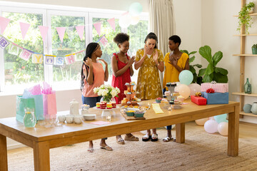 Admiring gifts and decorations, diverse female friends celebrating baby shower at home