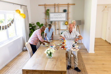 Senior diverse friends arranging cupcakes on table at home during retirement celebration
