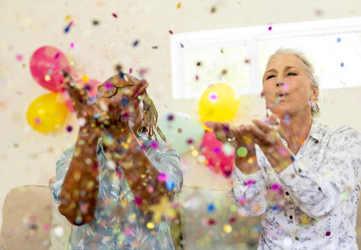 Celebrating with colorful confetti and balloons, senior diverse friends smiling joyfully at home
