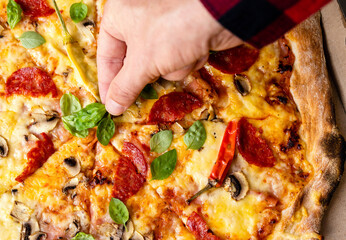 Hand adding basil leaf to freshly baked pizza