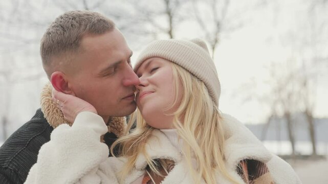 Happy couple in love walking together outdoors in a winter park. The husband tenderly kisses his wife during the walk.