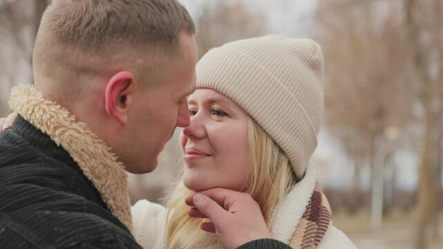 Happy couple in love walking together outdoors in a winter park. The man tenderly kisses his wife during the walk.