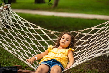 Cute little girl swinging and relaxing in hammock in backyard. Summer kids activity.