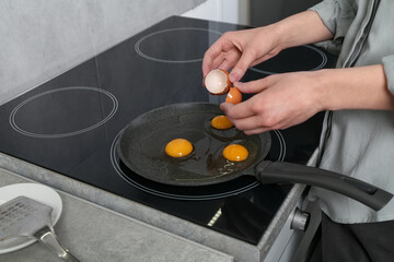 Woman breaking egg into frying pan in kitchen, closeup