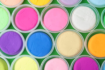 Different colorful modeling clay in plastic jars on green background, flat lay