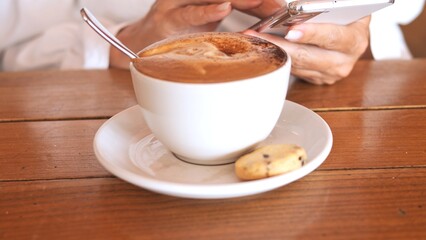 Tech-driven morning with warm cappuccino and smartphone Digital browsing social media and rich coffee aroma define modern way of enjoying daily coffee break with smooth foam and sweet treat 
