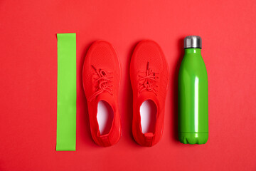 Elastic band, water bottle and sneakers on red background, flat lay. Sports equipment