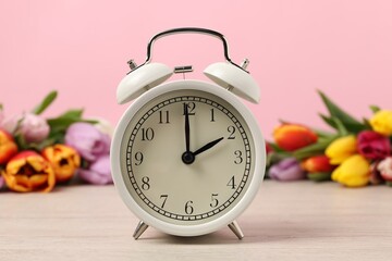 Spring time. Alarm clock and beautiful tulips on wooden table against pink background