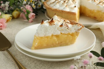Piece of delicious pie with browned meringue and flowers on light textured table, closeup
