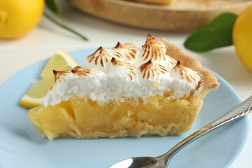 Piece of delicious pie with browned meringue, spoon and slice of lemon on white table, closeup