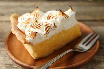 Piece of delicious pie with browned meringue and fork on wooden table, closeup