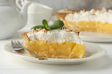 Piece of delicious pie with browned meringue, mint and fork on white wooden table, closeup