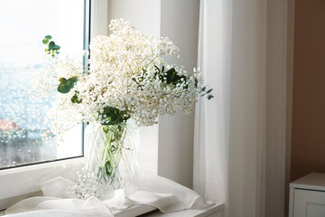 Bouquet of beautiful gypsophila flowers and eucalyptus branches in vase on window sill indoors