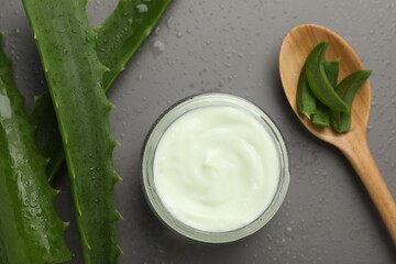 Moisturizing cream with extract of aloe vera in jar, cut leaves, spoon and water drops on grey background, flat lay