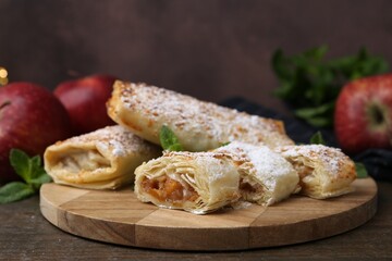 Tasty apple strudels with powdered sugar, mint and fruits on wooden table, closeup