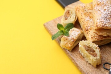 Tasty apple strudels with powdered sugar and mint on yellow background, closeup. Space for text