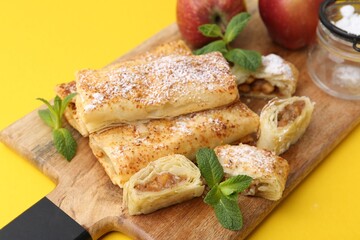 Tasty apple strudels with powdered sugar, fruits and mint on yellow background, closeup