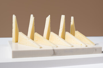 Trozos de queso de oveja curado. Queso manchego en un plato de mármol sobre fondo marrón