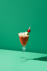 Cóctel Bloody Mary servido con crema de rábano picante adornado con tomate cherry y pepino sobre fondo verde	