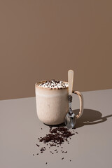 Café servido en taza con crema de leche y fideos de chocolate sobre fondo marrón