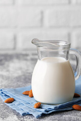Glass pitcher filled with milk sits on concrete countertop with blue napkin and almonds scattered around creating visually appealing scene promoting healthy eating