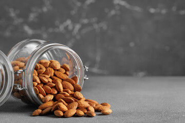 Shelled almonds spilling from glass jar onto gray surface, creating visually appealing arrangement...