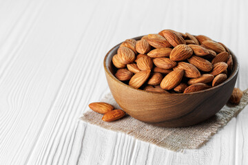 Shelled almonds are overflowing wooden bowl placed on small cloth napkin on white table, creating warm and inviting scene perfect for healthy snacking