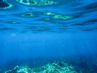Dark blue ocean surface seen from underwater. Abstract waves underwater and rays of sunlight shining through, Sun light rays undersea deep, Underwater background with sea bottom, Mediterranean sea.