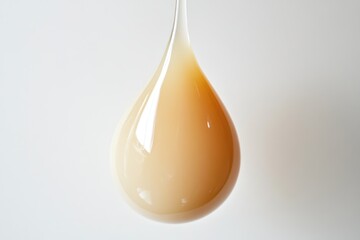 A single, teardrop-shaped droplet of light beige liquid hangs suspended against a white background.