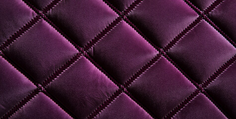 Fototapeta premium A close-up of a luxurious purple velvet fabric with a quilted pattern, highlighting its rich color and softness. The symmetrical diamond shapes add depth and texture to the surface, creating elegance.