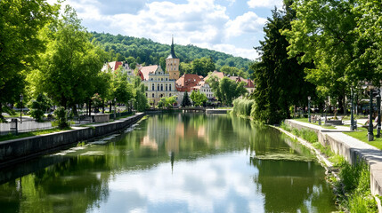 Scenic riverside town, charming architecture reflected in calm water, lush greenery, sunny day, ideal for travel brochures