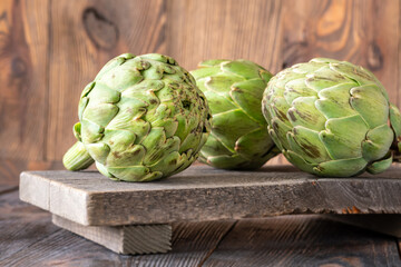 Fresh raw artichokes on vintage cutting board with rustic wooden background texture