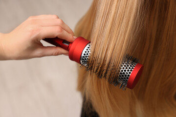 Hairdresser styling client's hair with round brush in salon, closeup