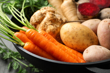 Different root vegetables in pot on black table, closeup