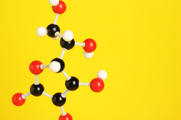 Molecule of vitamin C on yellow background, closeup and space for text. Chemical model