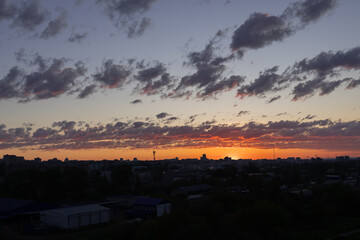 Amazing red sunset over the city. Silhouettes of houses. Cloudy sky