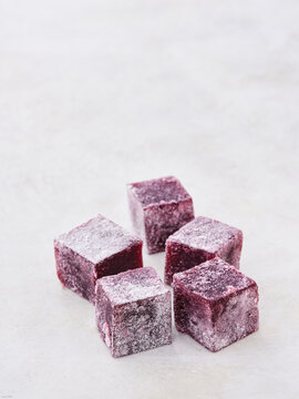 A charming display of soft, chewy berry cubes lies scattered on a light, textured surface