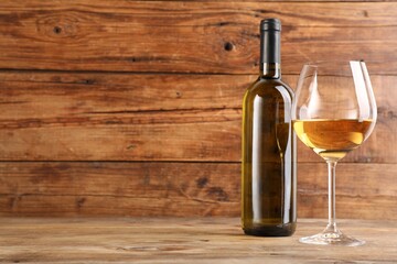Tasty white wine in glass and bottle on wooden table, space for text