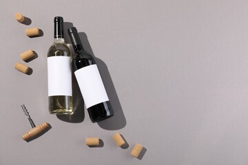 Bottles of wine, corks and corkscrew on light grey background, flat lay. Space for text