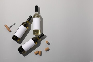 Bottles of wine, corks and corkscrew on light background, flat lay. Space for text