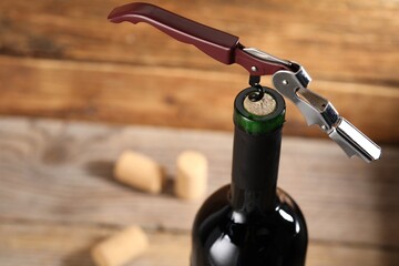 Bottle of luxury wine with corkscrew on blurred background, closeup. Space for text