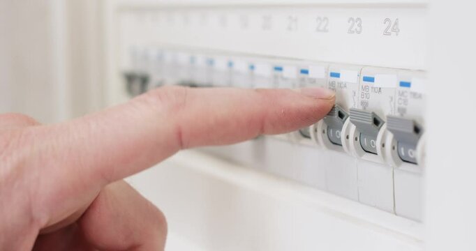 Man hand switches on circuit breaker on electrical panel in cabinet. Male electrician isolates electrical sections safely for repair work in building