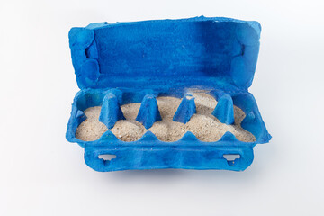 Open blue egg carton filled with sand, repurposing its compartments for a creative craft project....