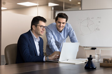 Two business professionals collaborate using laptop during brainstorming session in modern...