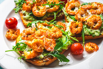 Toast or sandwiches with avocado oil, arugula and fried prawns on a white plate on a light blue background with a napkin. Healthy breakfast. View from above. Flat layout. Space for text.